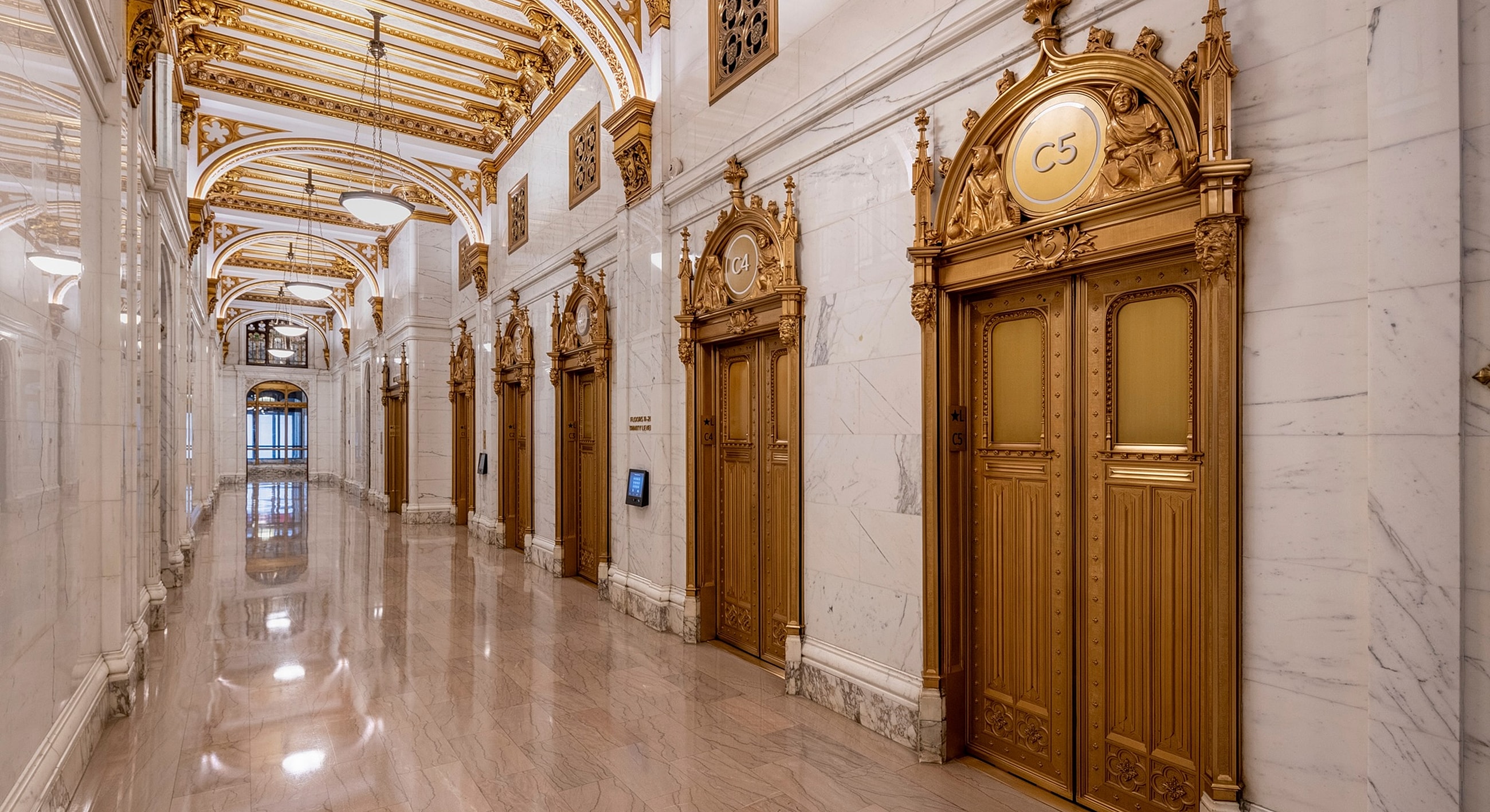 Lavish hallway with ornate golden elevator doors.